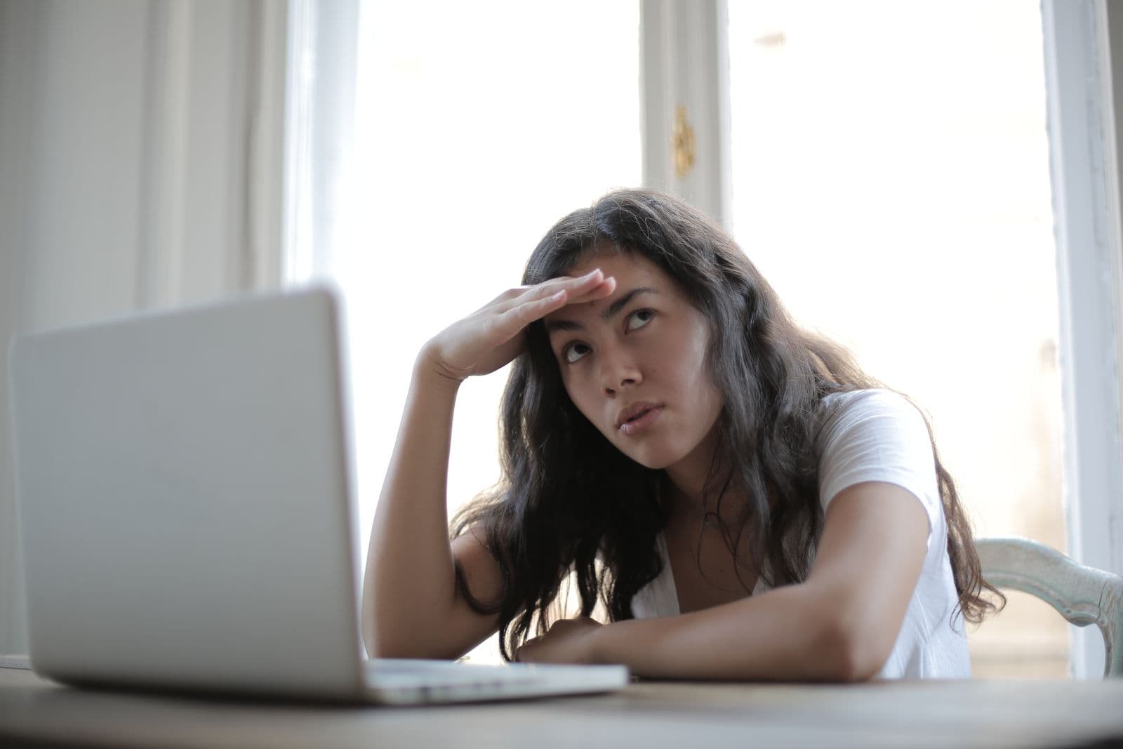Woman resting her head on her hand looking confused and frustrated while staring at a laptop screen