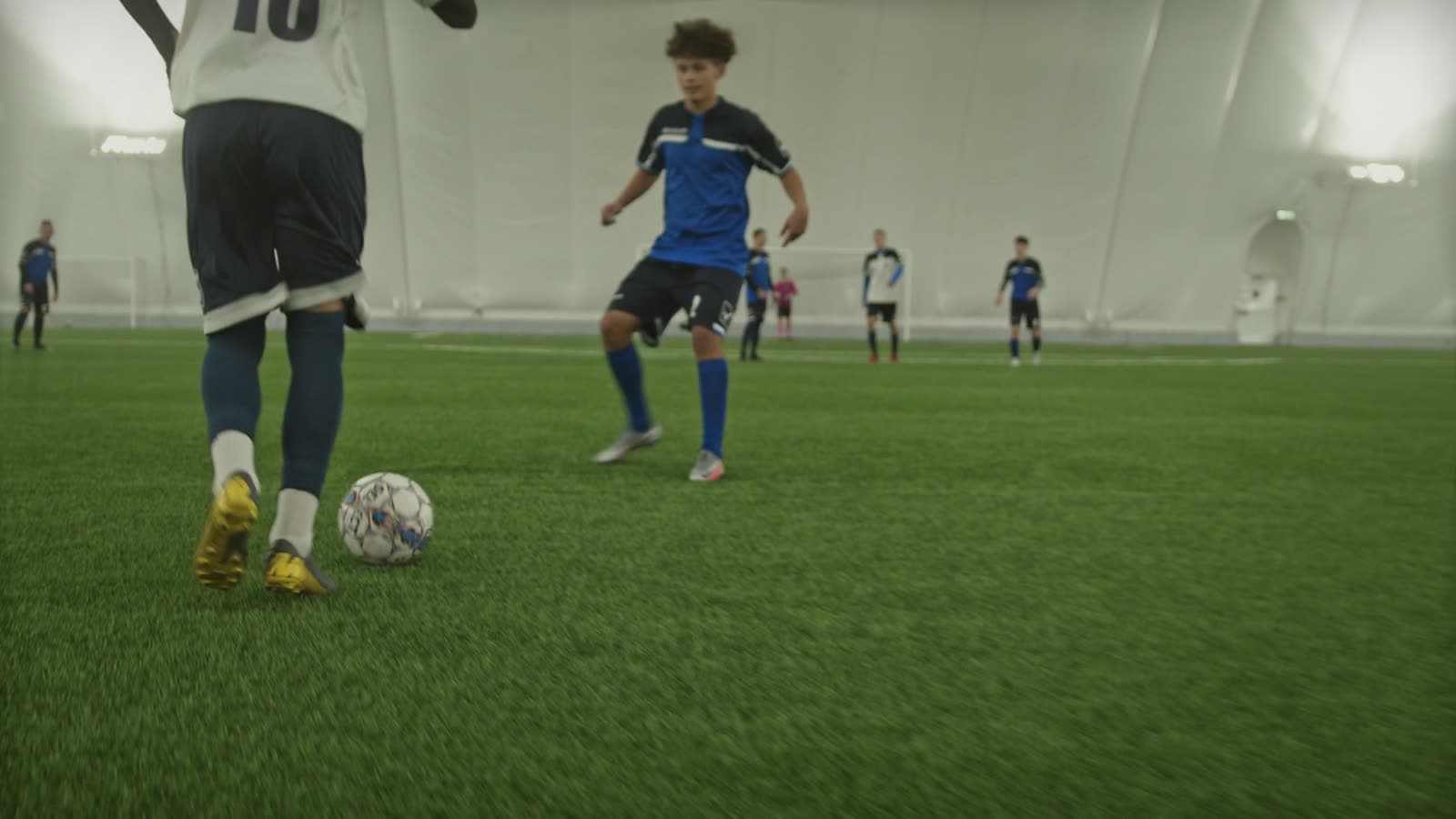 Indoor soccer dome with multiple adult players mid-game, viewed from pitch level