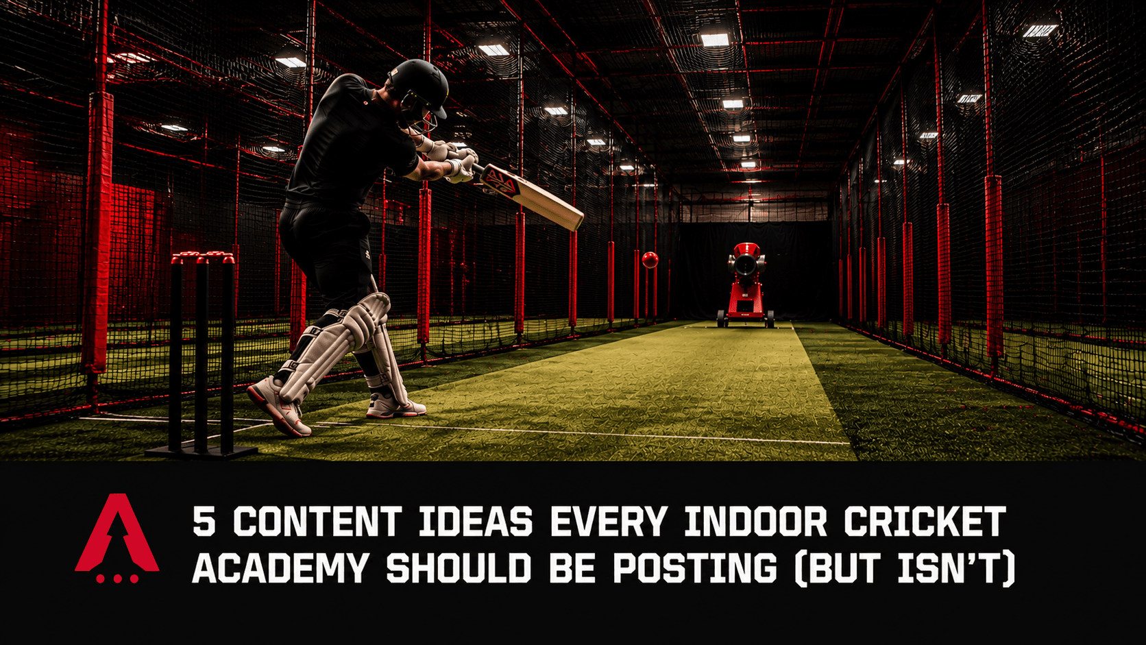 Batsman playing a shot in a dark indoor cricket net facility with a bowling machine and red netting in the background