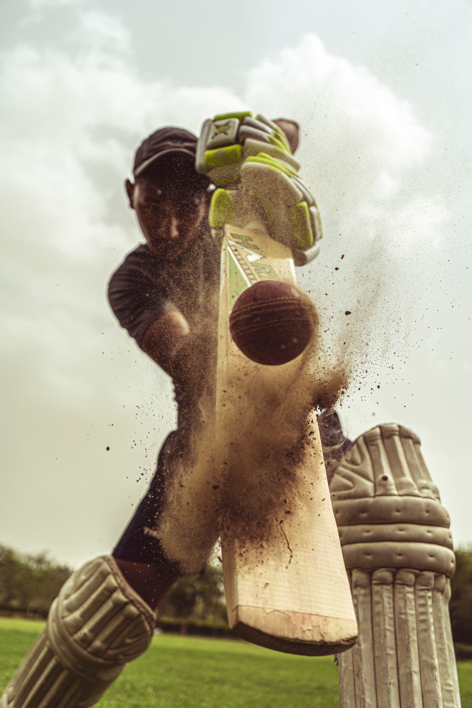 Cricket batter making powerful contact with the ball, dust flying