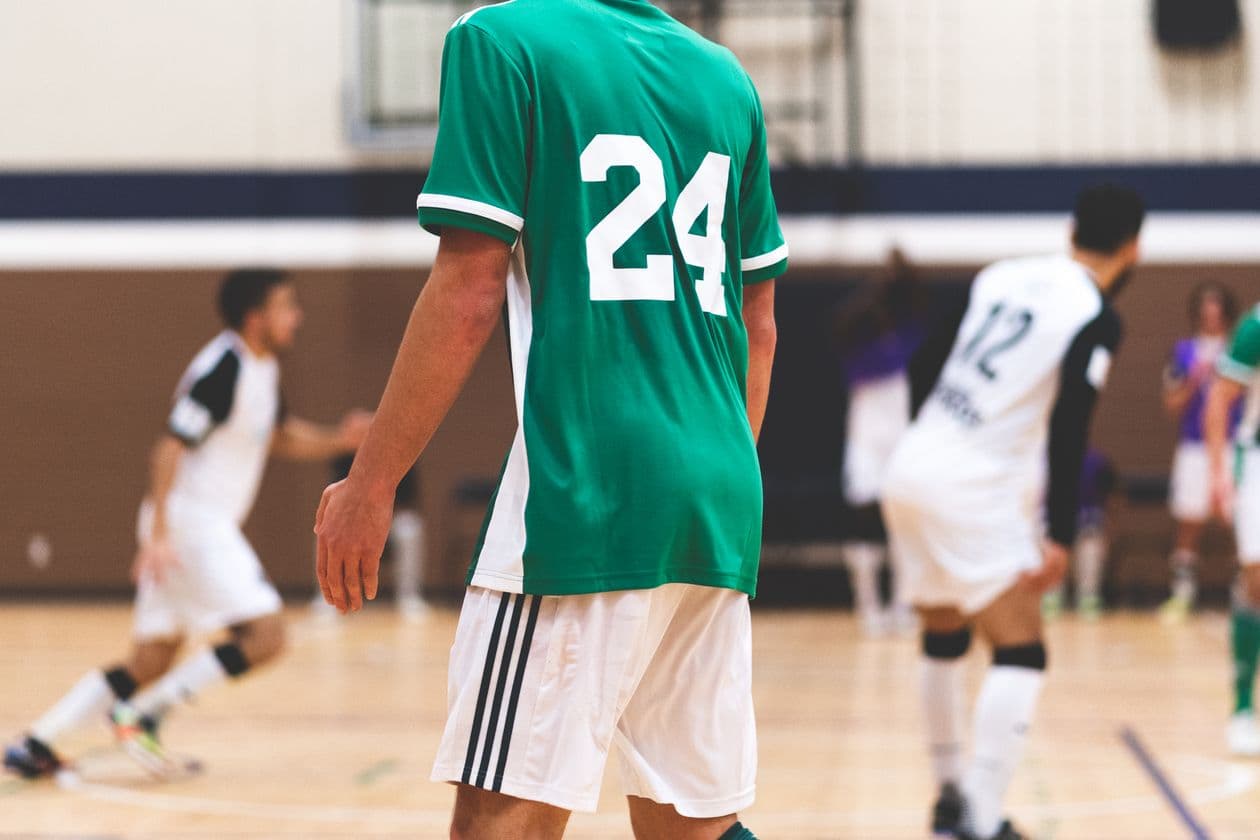 Indoor soccer players in green and white jerseys competing in an intense match inside a sports hall