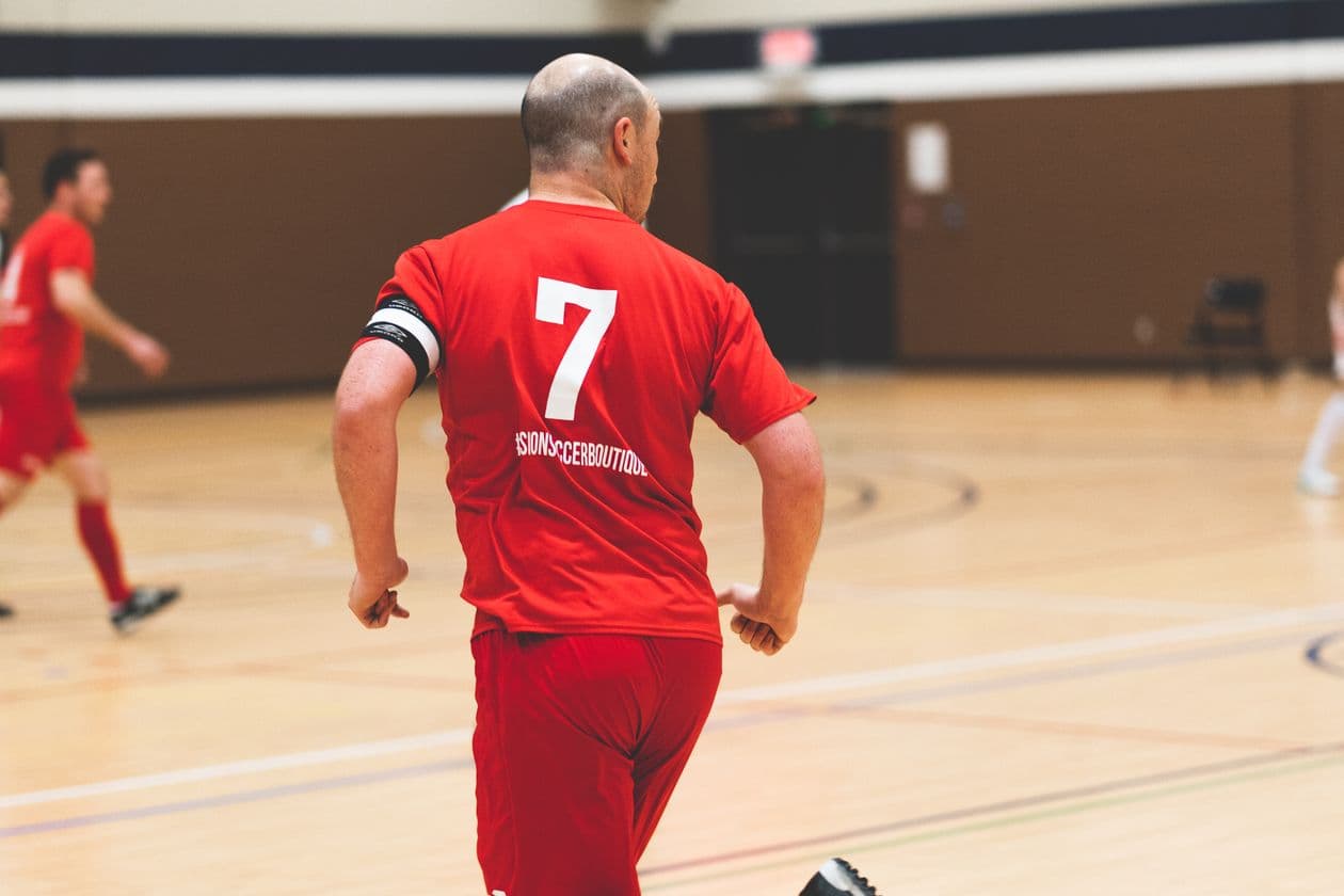 Man in a red jersey playing indoor soccer in a sports hall during a competitive match