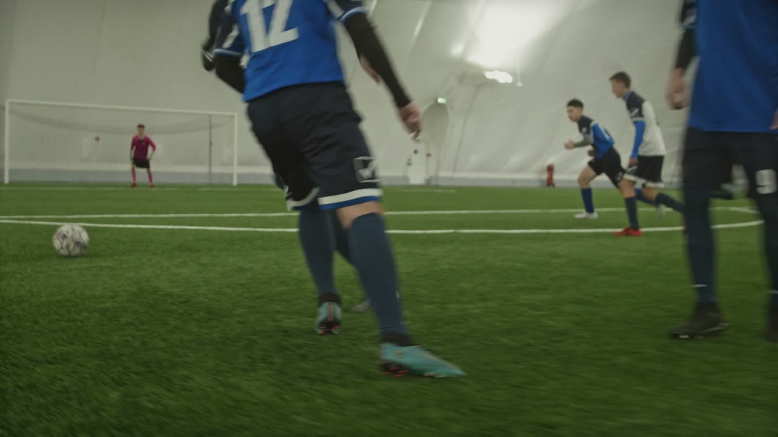 Youth soccer players in motion on turf inside an indoor dome facility, with the dome's arched structure visible