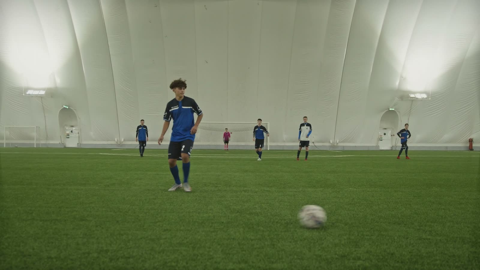 Youth soccer player on turf inside an indoor dome, with the full dome structure visible behind them
