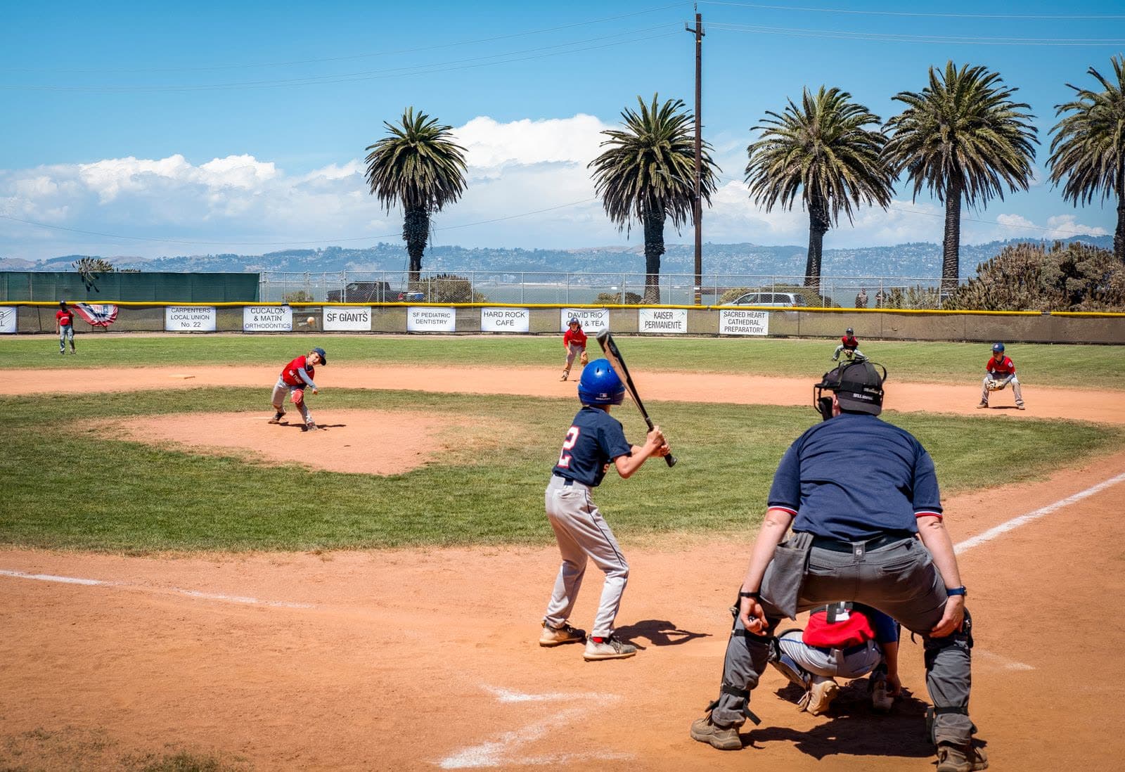 Youth Little League baseball game at bat with palm trees in the background