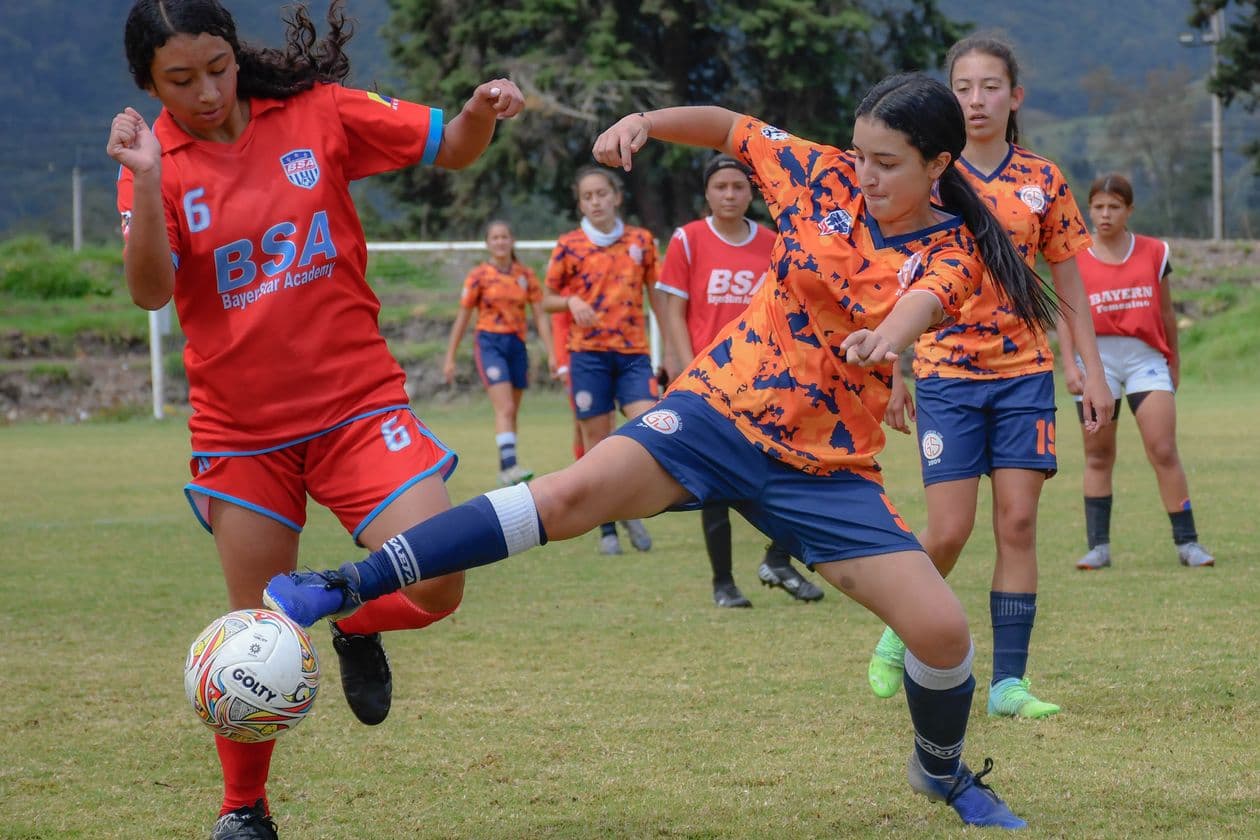 Girls soccer players competing in a match in orange and red jerseys